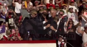 En la imagen Donald Trump saluda al público mientras baja de la tarima escoltado por varios miembros del equipo de seguridad